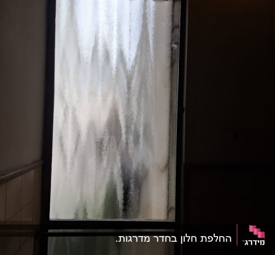 חלון זכוכית גלית ומטושטשת במסגרת כהה בחדר מדרגות